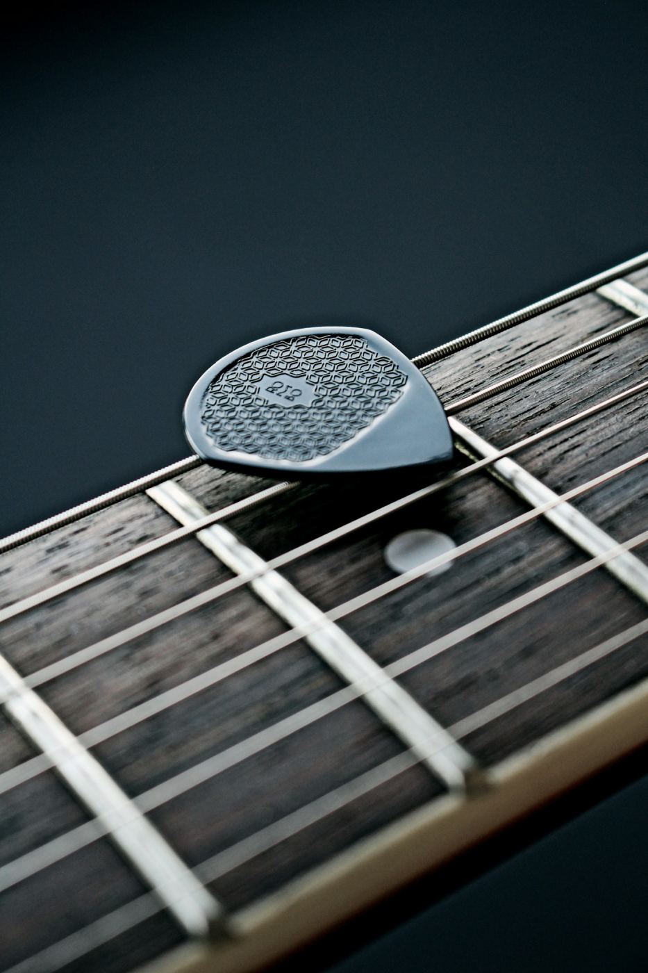 Close-up of frets and a pick on a fretboard